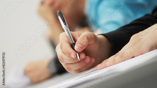 Fotografía A young man, a student or schoolchild, writes a dictation, an essay or solves an educational problem, sitting at a desk next to other students