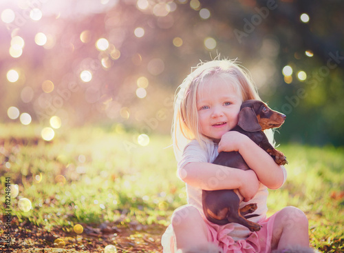 Portrait, outdoor and hug of puppy by toddler, adorable and cute in park, love and care for animal. Nature, little girl and child with pet, relax and embrace of dog, grass and together on ground photo