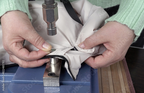 Close-up of the hands of a woman who puts rivets on outerwear and a jacket on a riveting machine photo