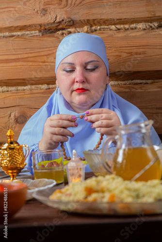 A Muslim woman in a blue hijab is fingering her rosary at the Iftar Ramadan table