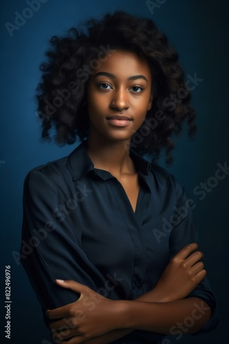 Young African American woman with curly hair in a dark shirt posing with folded arms against a blue background