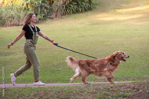 .young woman walking golden retriever dog in park on summer day