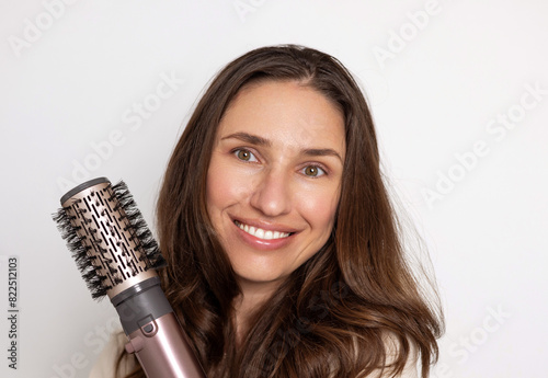 smiling woman using rotative hair brush to arrange or dry hair.isolated girl with beautiful natural hair and dryer in hand. happy satisfied female, advertising banner for care, styling product.