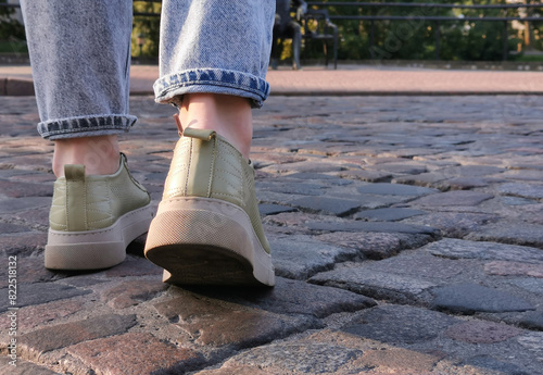 Close-up of a persons feet in sneakers walking on an old cobblestone path.