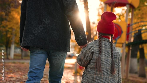 Little girl walks hand in hand with loving father through playground. Girl and father draw nearer to playground with interest. Girl and father go to playground to look at various play equipment photo
