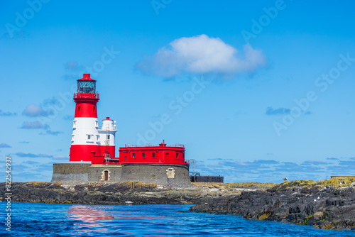 Longstone Lighthouse in the Outer Farne Islands on the Northumberland Coast, UK, with basking seal and seabirds on lichen covered rocks.  Horizontal.  Space for copy.