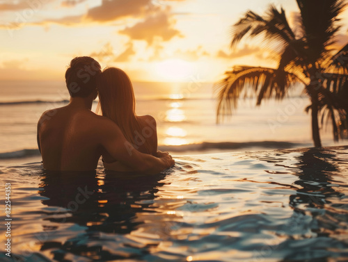 Seascape sunset with a couple hugging and sitting on the border of a swimming pool in a tropical resort  enjoying the sunset over the sea during the summer vacation on the sea.