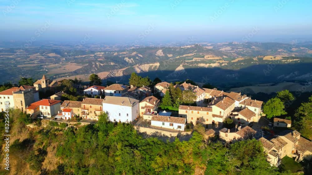 Delightful aerial push-in fly-over shot from Smerillo (Fermo) featuring the village and its houses, buildings and church, interspersed with trees, perched on a tall cliff with a mountainous background Delightful aerial push-in fly-over shot from Smerillo (Fermo) featuring the village and its houses, buildings and church, interspersed with trees, perched on a tall cliff with a mountainous background