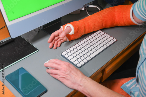 woman with broken right arm in a plastic orange cast works with her left hand on a computer, temporary disability,high quality photo