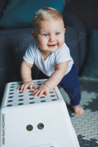 A small child in a white bodysuit is learning to crawl on a clean, heated floor. Home photo of a cute blue-eyed baby.