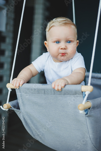 Baby boy swings on a swing at home. A child rides on a swing at home