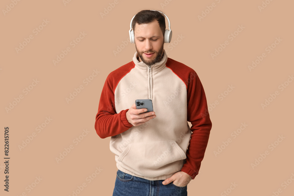 Young man in modern headphones with mobile phone on brown background