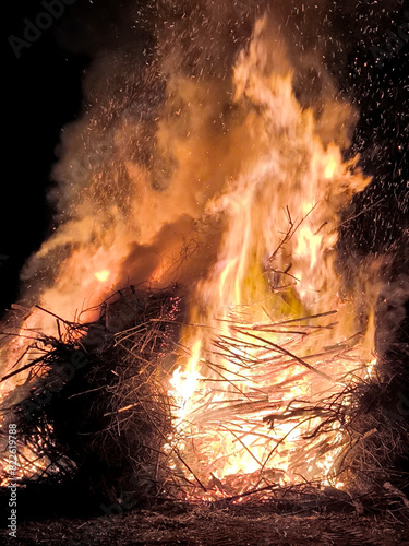 A huge easter fire blazes at night, captivating a crowd with the flames, under a dark sky