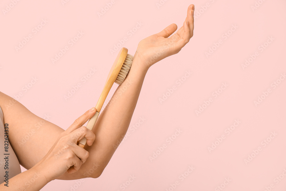 Young woman massaging her arm with body massage brush on pink background Young woman massaging her arm with body massage brush on pink background