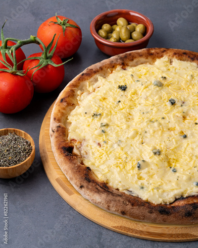 Four cheese style pizza over stone background with tomatoes, olives and oregano