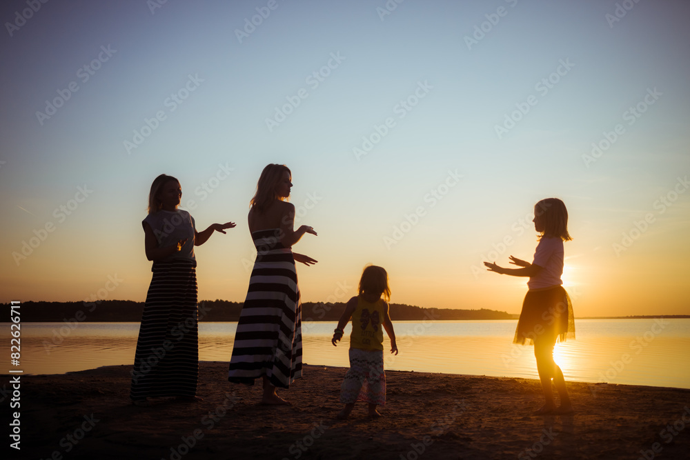 Silhouette of groupe dancing people at sunset. Childhood and motherhood happiness concept. Women and children. Summertime season. Joyful emotions. Summer vacation. Holidays. Birthday mood. Seascape