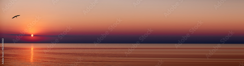 A abstract banner of serene sunset over a calm ocean with birds flying in the sky. The sun dips below the horizon, casting a warm glow over the landscape.
