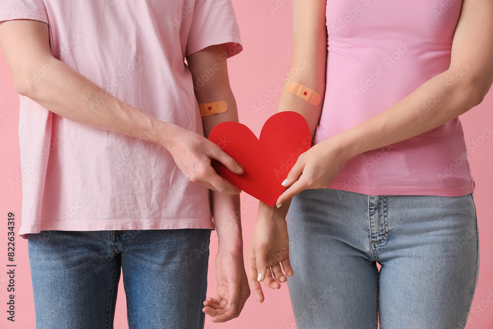 Blood donors with applied patches and paper heart on pink background, closeup Blood donors with applied patches and paper heart on pink background, closeup