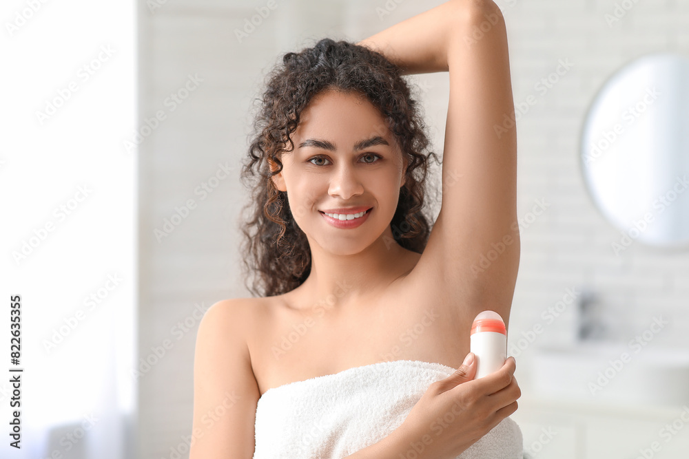 Naklejka premium Beautiful young African-American woman with deodorant in bathroom