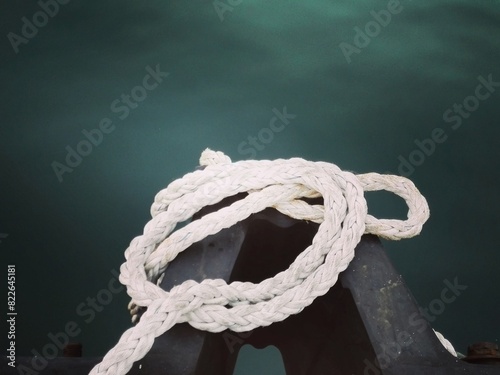 White sail ship rope against dark blue sea. Mooring bollard with unfixed rope on ship or boat. Close-up of nautical mooring rope on ship or sailboat. Marine yacht knot detail on stainless steel anchor photo