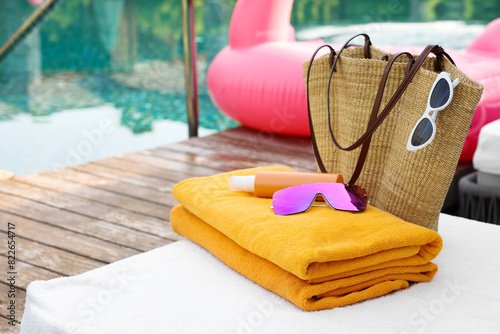 Fototapeta Naklejka Na Ścianę i Meble -  Wicker bag with beach accessories on sun lounger near outdoor swimming pool, space for text. Luxury resort