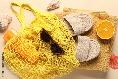 String bag, different beach accessories and orange on beige background, top view