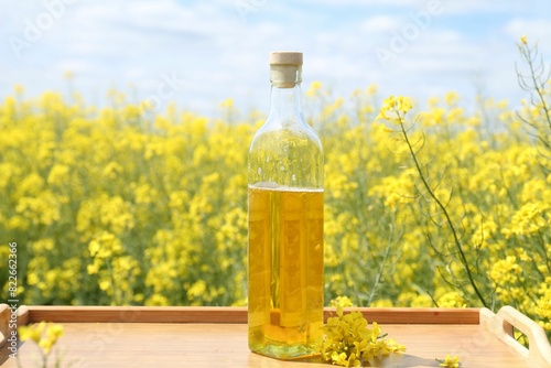 Rapeseed oil in bottle on tray in field, closeup