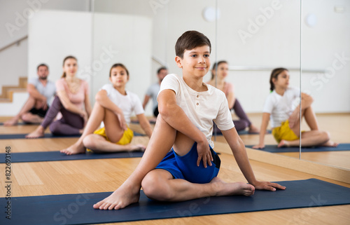 Young boy exercising lord of the fishes pose with her family during group yoga training.