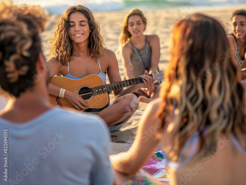 Beautiful woman sitting on the sandy beach is playing a guitar for the friends around her during the sunset.