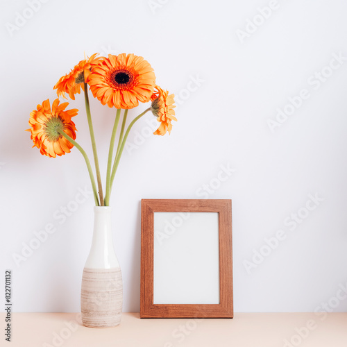 Blank picture frame and orange gerbera flowers in vase on the white background. Holiday, Women's Day or Mother's Day concept