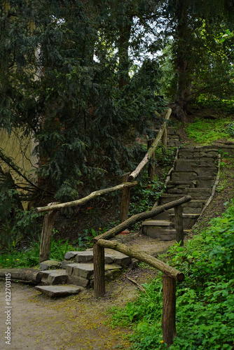 Forest path with stone steps and wooden railings, with green trees and shrubs, atmosphere of seclusion and tranquility, creating sense of immersion in forest world, with authentic, rustic appearance.