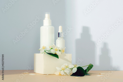 Cosmetic toner and serum in empty packages on a podium against a white wall background with light and shadows. Natural skin care products concept