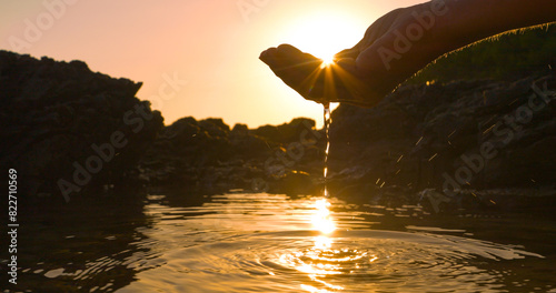 Foto CLOSE UP, LENS FLARE: Sunbeams peep through a hand scooping water in sea puddle formed at low tide on rocky shore