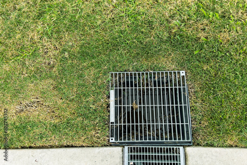 Top view of metal grate of water drainage system for storm water drainage from a pedestrian sidewalk in park.