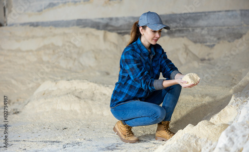 Woman agronomist squatting at bunch of corn flour inside of fodder storage. © JackF