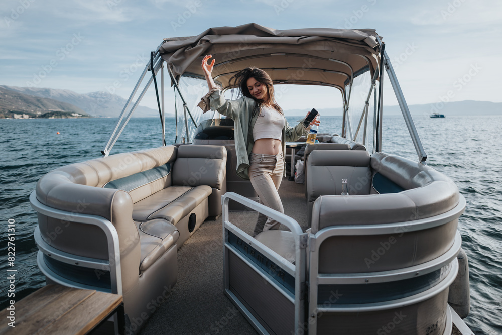 Naklejka premium A happy, joyful girl raises her arms in celebration while standing on a pontoon boat, surrounded by beautiful mountain and water landscapes.