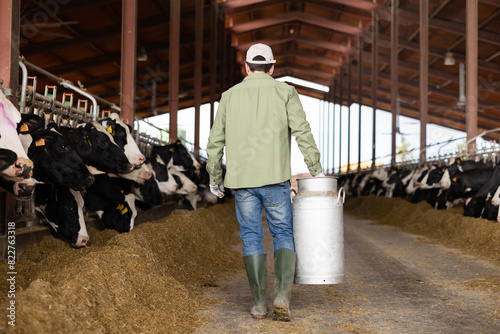 Male farmer carries a large milk can in his hands at a cow farm photo