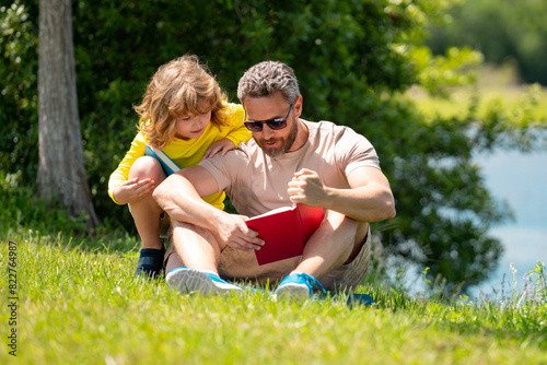 Father and son reading a book in park. The concept of education and friendship. Lifestyle, father read a book to his cute son outdoors, warm summer day, family relationship, child and parent, single © Volodymyr