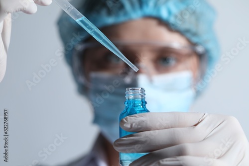 Scientist dripping liquid from pipette into glass bottle on light background  closeup