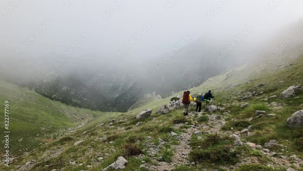 Backpackers trek along a scenic mountain trail, surrounded by lush greenery and rocky terrain, under a bright blue sky with scattered clouds. Backpackers trek along a scenic mountain trail, surrounded by lush greenery and rocky terrain, under a bright blue sky with scattered clouds.