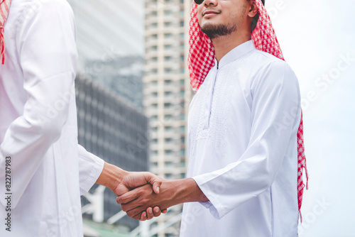 Islamic businessman shake hands together dealing success business in modern muslim UAE city. Arab man wear hijab muslim dress. Multicultural diversity business people meeting talking group cityscape