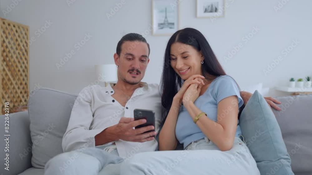 Caucasian young couple sitting on sofa and swipe mobile phone in house. Caucasian young couple sitting on sofa and swipe mobile phone in house.