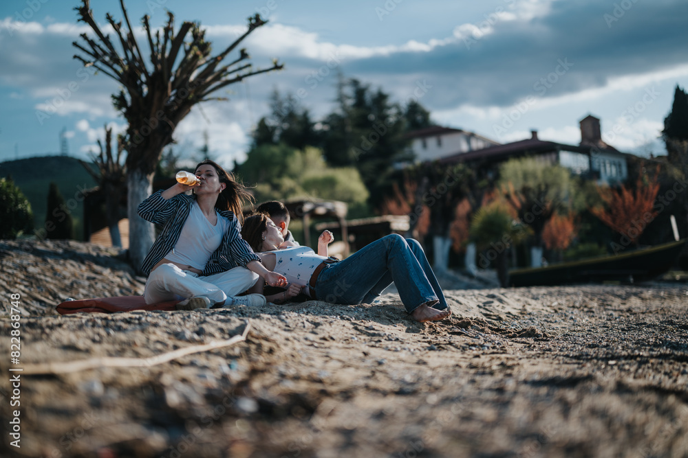 A young couple relaxes on a sandy beach, enjoying a moment together with a glass of wine, surrounded by serene nature and quaint buildings. A young couple relaxes on a sandy beach, enjoying a moment together with a glass of wine, surrounded by serene nature and quaint buildings.