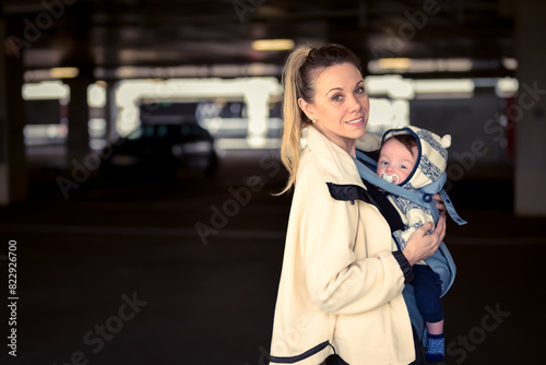 Sideview of a happy woman looking and smiling to camera while holding and carrying her baby