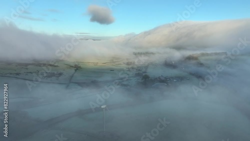 Misty landscape with mountain covered in flowing cloud at dawn in winter. Spinning wind turbine in foreground. Above the clouds. English Lake District, Cumbria, UK. photo