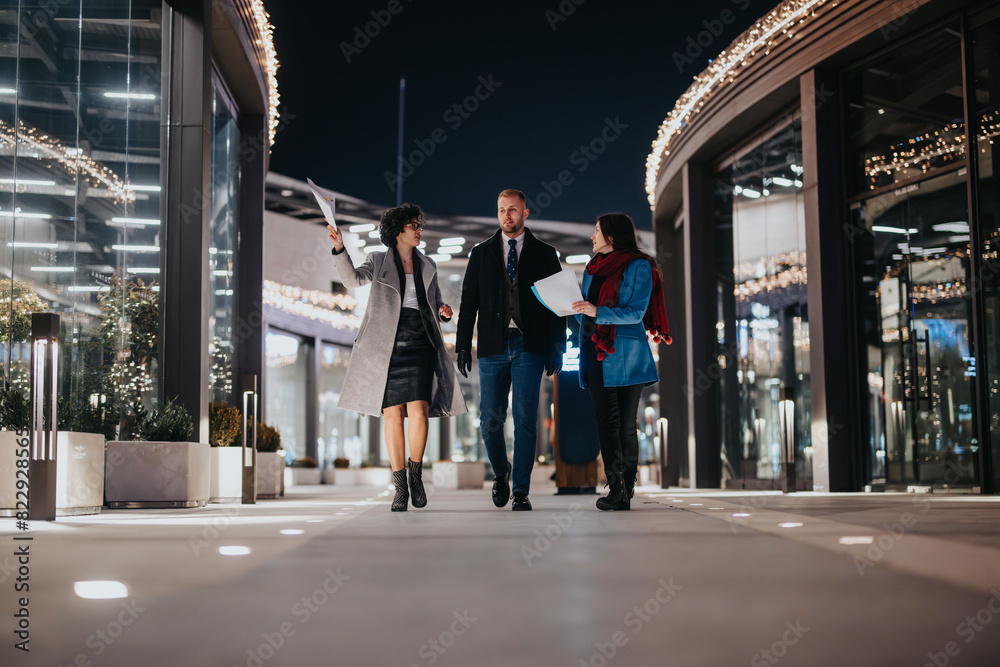 Business colleagues confidently walk outdoors at night, engaged in conversation with documents in hand, illuminated by city lights.