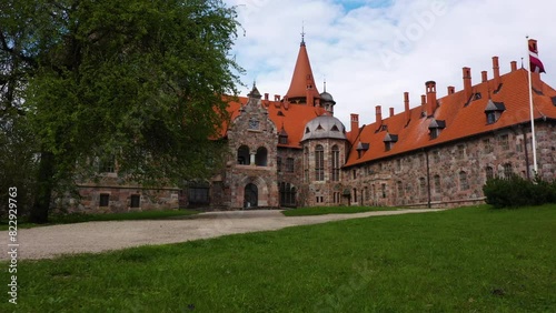 Cesvaines castle with Latvia flag on grassy grounds with dirt driveway entrance photo