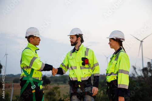 Team engineer wearing safety uniform shake hand discussed plan about renewable energy at station energy power wind. technology protect environment reduce global warming problems.