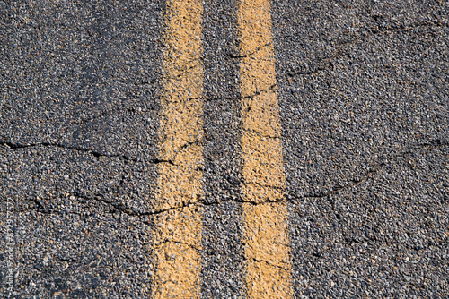 Solid yellow lines on road with cracks on desert highway.