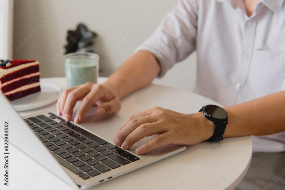 Hands typing on a laptop with a slice of cake on a white table, creating a cozy work environment. Hands typing on a laptop with a slice of cake on a white table, creating a cozy work environment.